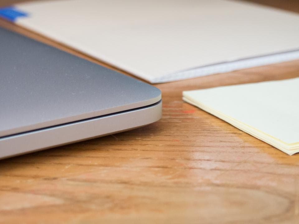 Un portátil gris cerrado, una libreta y un taco de notas adhesivas sobre una mesa de madera: comparar dos programas de gestión antes de elegir