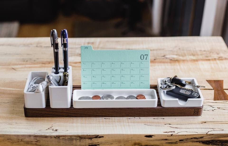 Un calendario de sobremesa con las casillas de un mes, apoyado en un organizador de madera con bolígrafos, monedas y llaves: el calendario de Verifactu se desplaza
