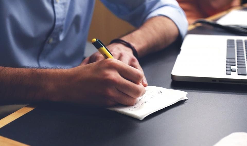 Persona escribiendo a mano sobre un papel junto a un portátil: facturar a mano es uno de los casos que dejan fuera de VeriFactu